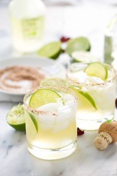 two glasses filled with margarita cocktails on top of a white marble counter next to nuts