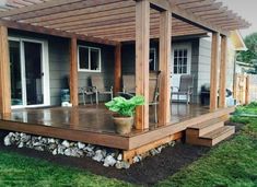 a wooden deck in front of a house with plants on the ground and chairs around it