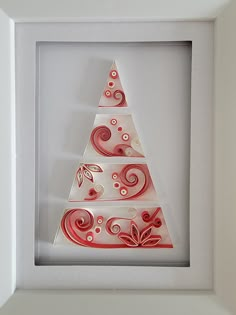 a paper christmas tree is in a white frame with red swirls on the bottom