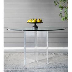 a glass table with fruit on it and a plant in the corner next to it