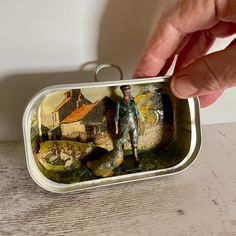 a hand holding an empty tin with a painting on it