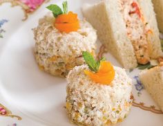 three small sandwiches on a plate with orange garnishes