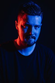 a man in black shirt looking at something with blue light on his face and dark background