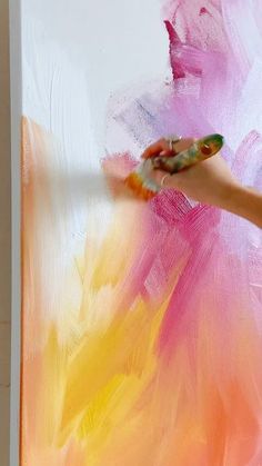 a person is painting on the wall with pink and yellow paint