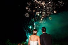 a bride and groom looking at fireworks in the night sky