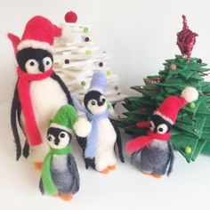 three stuffed penguins are standing next to a christmas tree and small toy penguines in hats