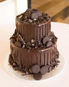 a three layer chocolate cake with cookies and oreo pieces on the top, sitting on a table