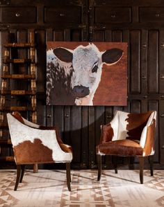 two brown and white chairs in front of a cow painting