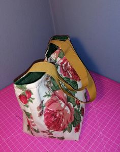 a flowered purse sitting on top of a pink table next to a purple wall