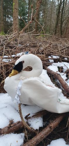 a white duck laying on top of snow covered ground next to some sticks and branches