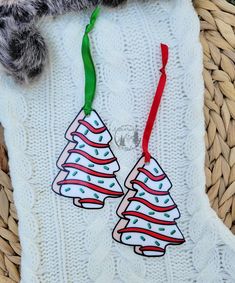 two christmas trees are hanging on a white knitted blanket with red and green ribbon