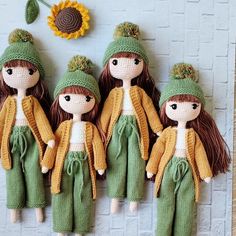 four little dolls with knitted hats and green pants are standing next to a sunflower