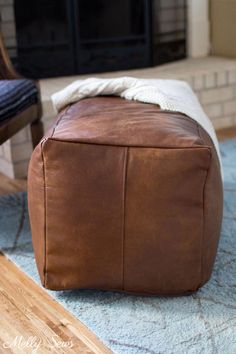 a brown leather ottoman sitting on top of a blue rug in front of a fireplace