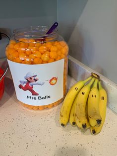 some bananas and oranges sitting on a counter top next to a jar of fire balls