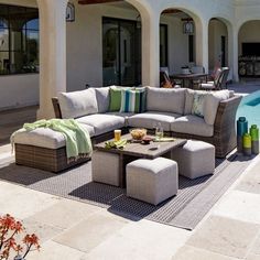 a couch and ottoman sitting on top of a patio next to a swimming pool in front of a house