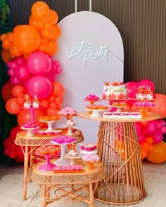 an assortment of desserts displayed on tables in front of a backdrop with orange and pink balloons