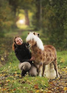 a woman kneeling down next to a brown and white horse