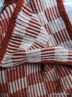 an orange and white knitted blanket laying on top of a bed