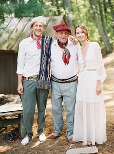 three people standing next to each other in front of trees and dirt ground with one person wearing a red hat