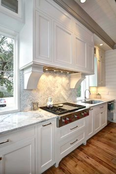 a kitchen with white cabinets and wood flooring next to a stove top oven under a window