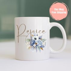 a white coffee mug with blue flowers and the word rejoce printed on it