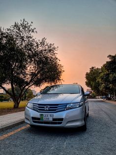 a silver car is parked on the side of the road near some trees at sunset