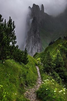 a path leading to the top of a mountain with clouds in the sky above it