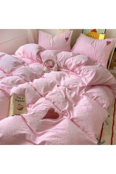 a bed with pink comforter and pillows on top of it next to a book