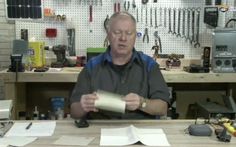 a man sitting at a table working on some construction material in his workshop with lots of tools