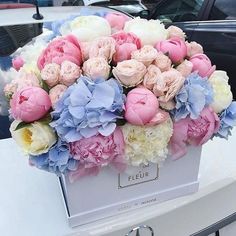 a bouquet of pink and blue flowers in a white box on the hood of a car