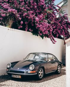 a black car parked in front of a white wall with purple flowers growing on it