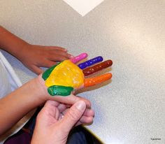 a person holding a plastic hand made to look like a rainbow colored bird with five fingers