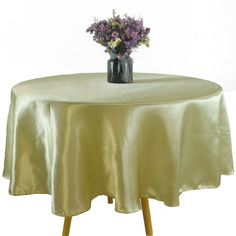 a vase with some flowers on top of a round table covered in a satin cloth