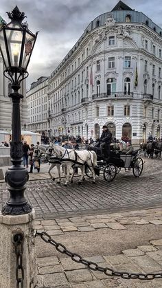 a horse drawn carriage traveling down a street next to a tall white building on a cloudy day