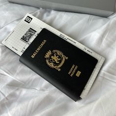 a black and gold passport sitting on top of a white bed next to a laptop