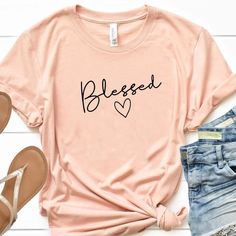 Blessed T-Shirt | Wear this t-shirt with pride knowing that a % of your purchase goes towards spreading the word of God. Part will go to building new churches, and part will go to sending missionaries around the world. Our Blessed T-Shirt is not only adorable but extremely soft too! Its bold Message will be sure to turn heads!  #tshirt #womenstshirt #womensfashion #christianapparel #tshirtforwomen #Love #God #Clothes #Christ #valerymilano God Clothes, Jesus Tees, The Word Of God, Indie Fashion, Christian Clothing, Christian Shirts, Word Of God, Brand Names, Room Ideas