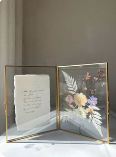 an open glass box with flowers in it and a poem written on the inside is sitting on a table