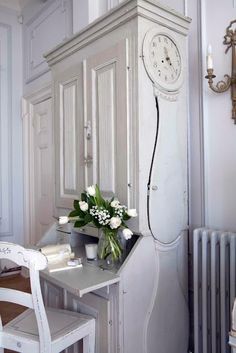 a room with white furniture and a clock on the wall next to a table that has flowers in it