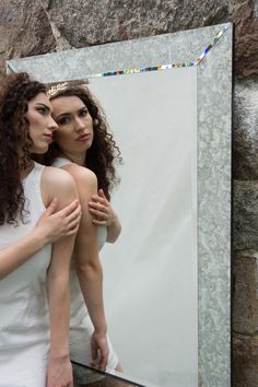 two women standing in front of a mirror with their arms around each other, both looking at themselves