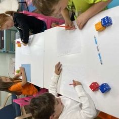 children are playing with magnets on a white board while others watch from the back