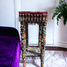 an ornate chair with beads and tassels on it in front of a purple velvet bed