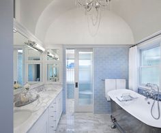 a large bathroom with blue and white tile on the walls, tub, sink and chandelier