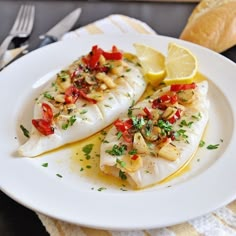 two fish on a white plate with lemon wedges