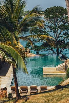 an outdoor swimming pool with lounge chairs and palm trees next to it on the beach