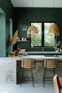 a kitchen with green walls and two stools in front of the counter top that has plants on it