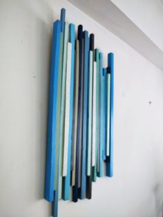 a blue and green wall hanging on the side of a white wall with sticks sticking out of it