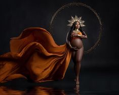 a pregnant woman wearing an orange dress and gold crown standing in front of a black background