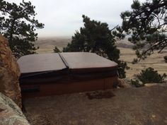 a hot tub sitting on top of a rocky hill next to trees and mountains in the background