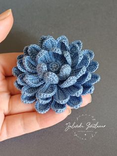 a crocheted blue flower is held in someone's hand on a gray surface