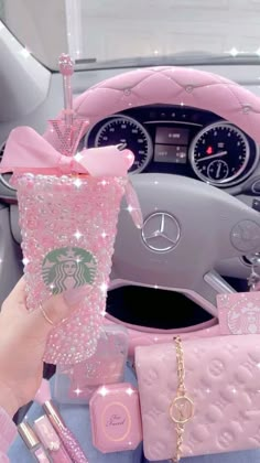 a person holding up a pink starbucks cup in their hand next to a car steering wheel